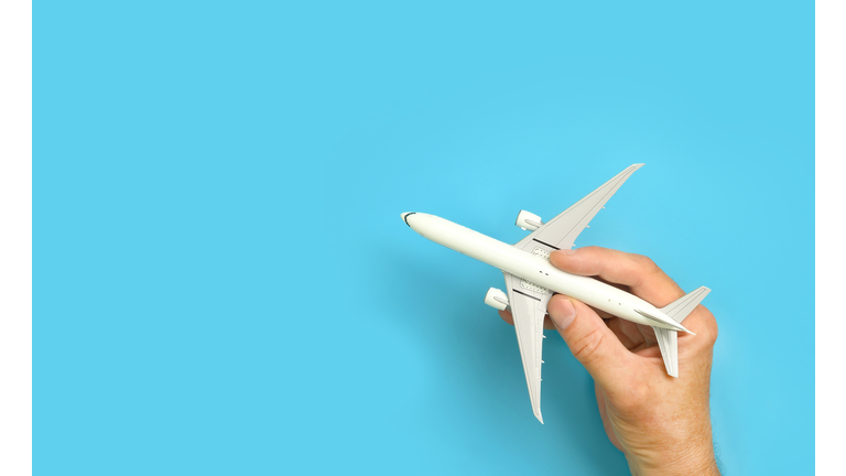 Male hand holding aircraft model, airplane in hand on blue background.