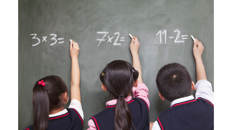 Three school children doing math equations on the blackboard