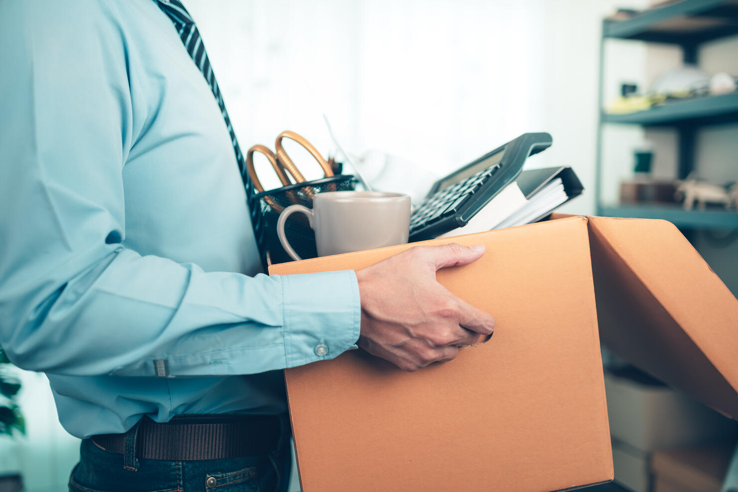 Unemployed hold cardboard box and resignation letter, dossier, alam clock, coffee cup, calculator and drawing tube in box. Quiting a job, businessman fired or leave a job concpet.