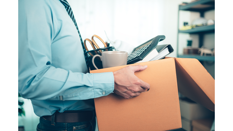 Unemployed hold cardboard box and resignation letter, dossier, alam clock, coffee cup, calculator and drawing tube in box. Quiting a job, businessman fired or leave a job concpet.