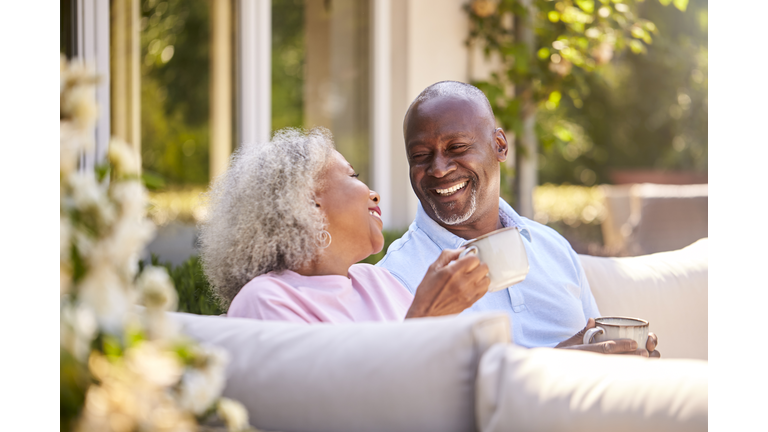 Retired Couple Sitting Outdoors At Home Having Morning Coffee Together