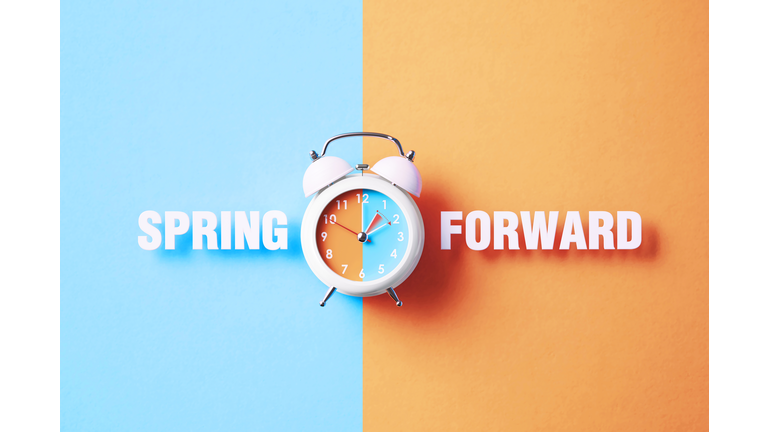 Spring Forward Reads Next To A White Alarm Clock On Blue And Salmon Background