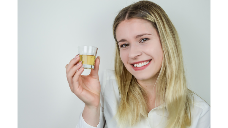 Portrait of a smiling beautiful young blonde woman holding a shot of liqueur