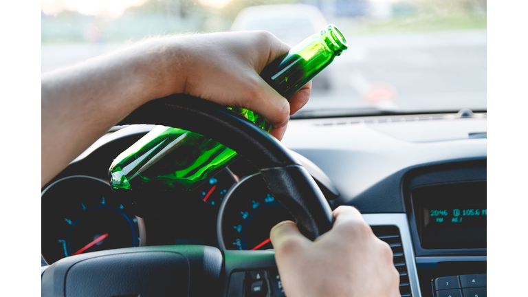 A man driving a car with a bottle of beer