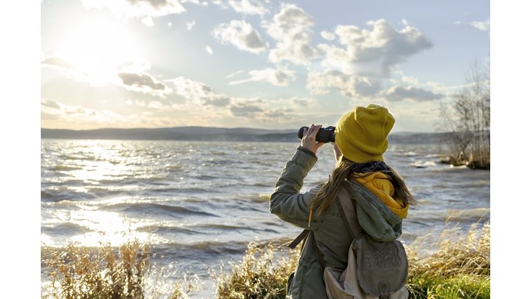 Young woman watching birds with binocular on lake. Scientific research
