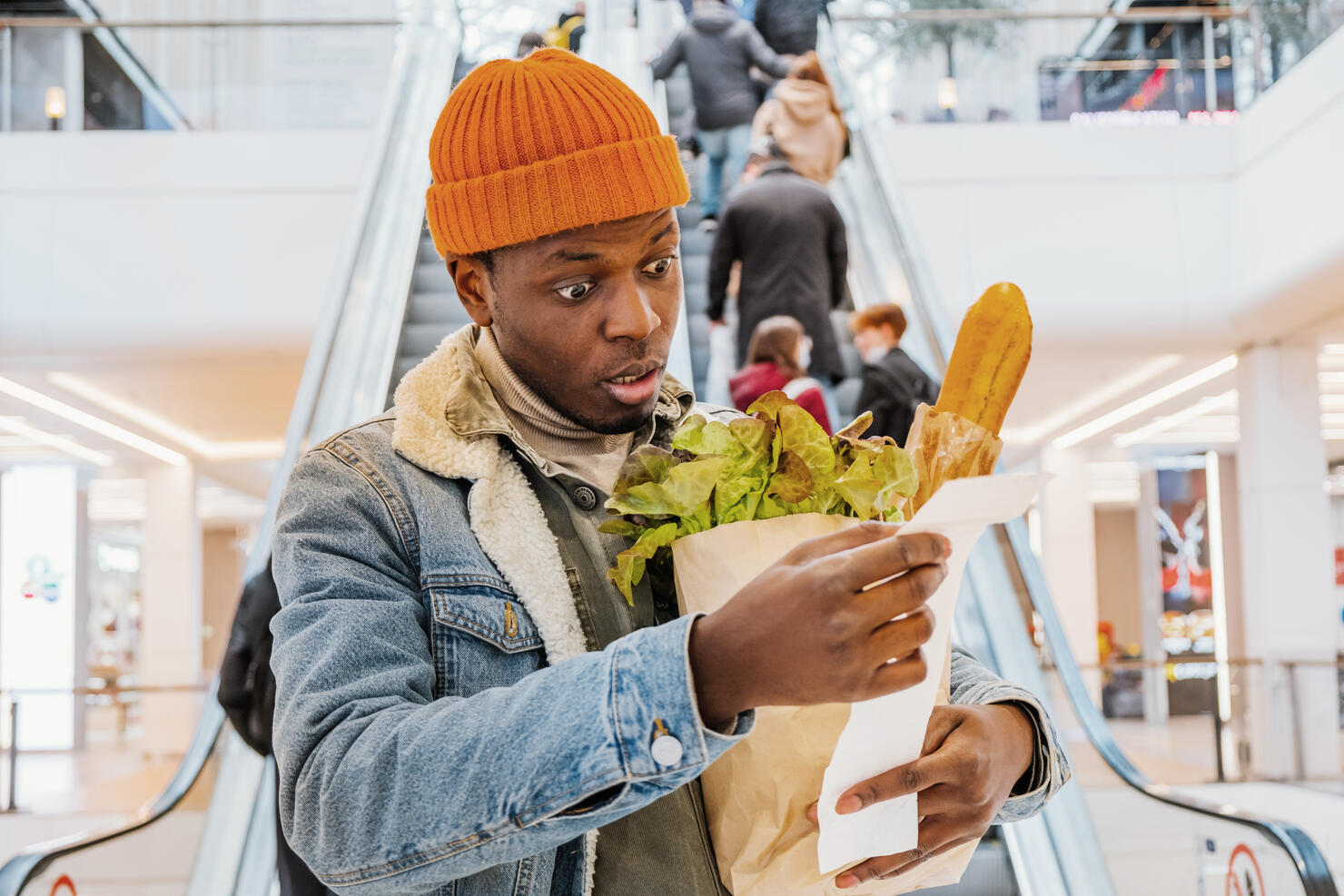 African man with a bag of groceries looks surprised and upset at a receipt from a supermarket with high prices. The rise in the price of food