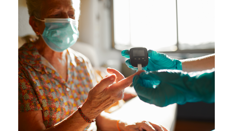 A nurse helping a senior woman perform a diabetes test