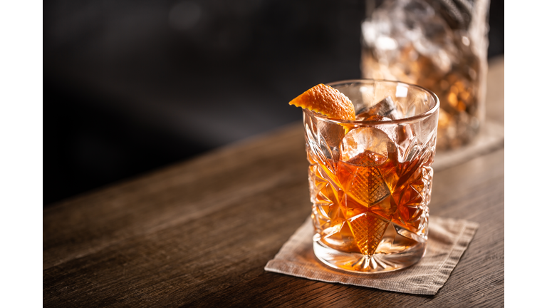 Old fashioned whiskey drink on ice with orange zest garnish.