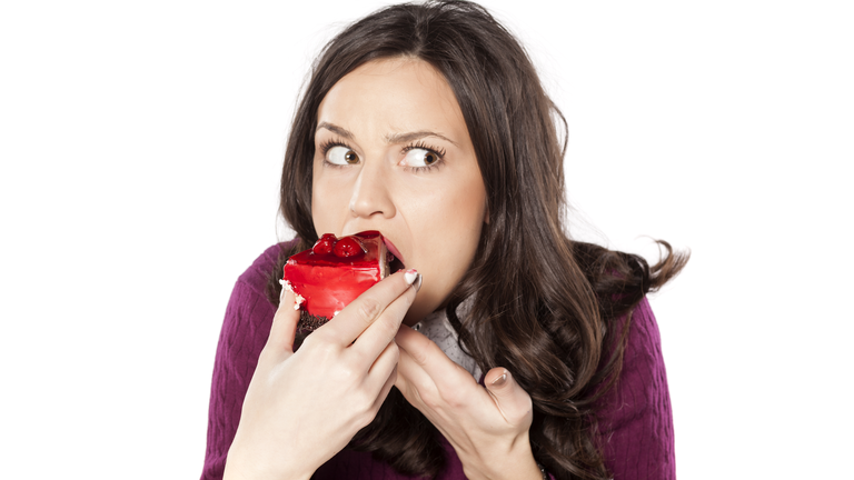 A woman eating a strawberry cake looking guilty