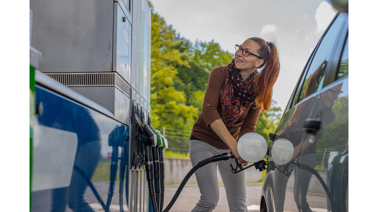 Happy woman refueling car looking at the machine.
