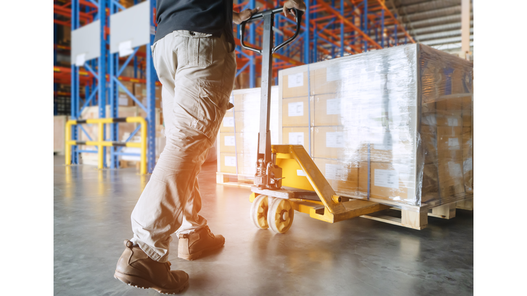 Warehouse worker is working with hand pallet truck and cargo pallet