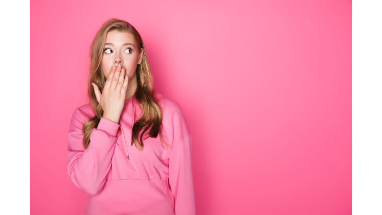 shocked beautiful woman covering mouth on pink background