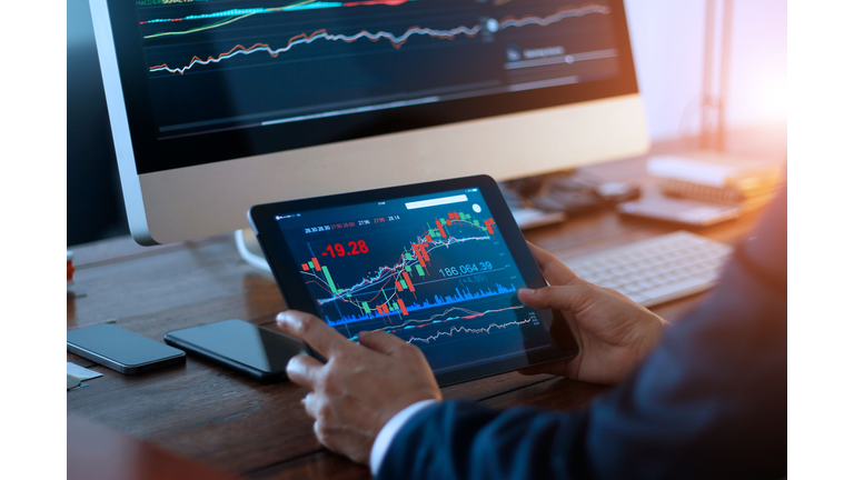 Businessman checking stock market on digital tablet and a desktop computer with stock exchange graph on screen. Financial stock market. Analyzing data in office background.