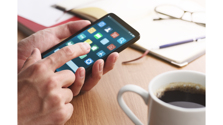 Closeup of male hands touching smartphone screen for using app at table.