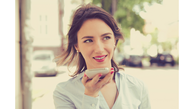 Woman using a smart phone voice recognition function online walking on a city street