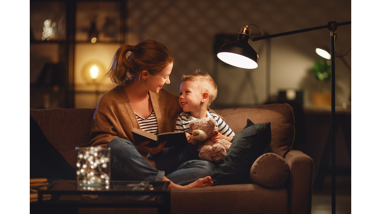 Family before going to bed mother reads to her child son book near a lamp in the evening