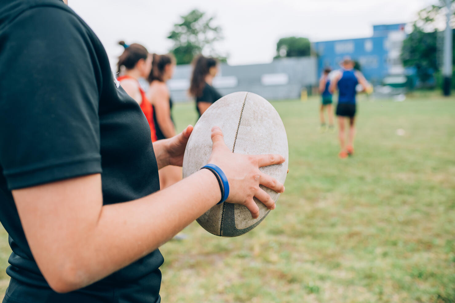 A group of women and their male coach at rugby training, one woman holding a rugby ball.