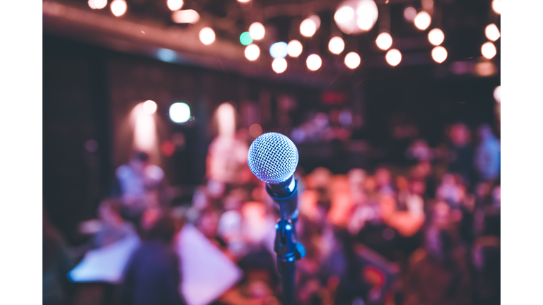 Event hall: Close up of microphone stand, seats with audience in the blurry background