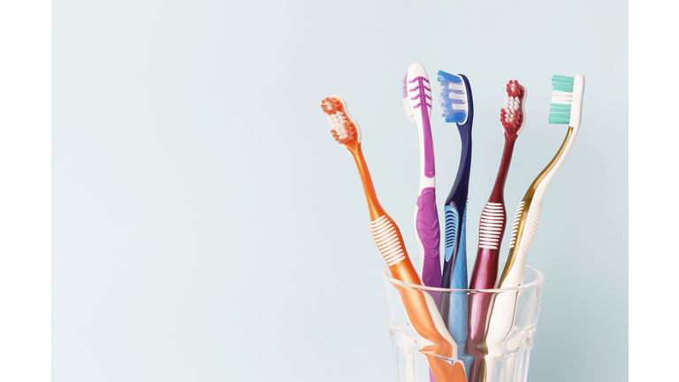 Multi-colored toothbrushes in a glass cup, blue background