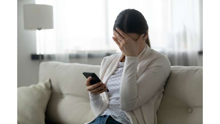 Stressed woman holding smartphone feels humiliated, cyberbullying concept