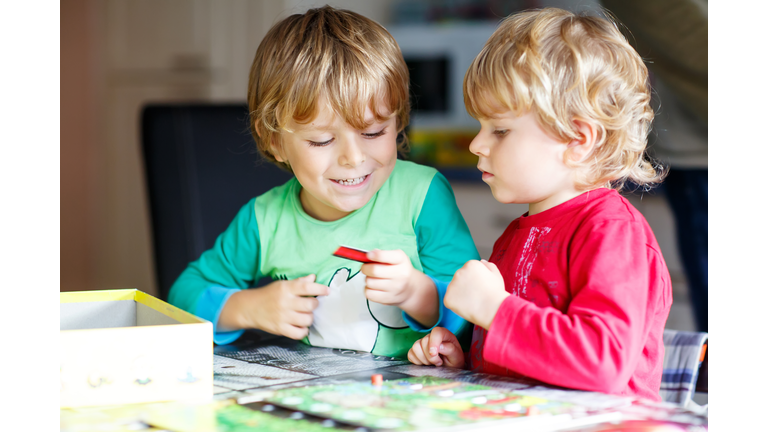 Two little blond kid boys playing together board game at home. Funny siblings having fun.