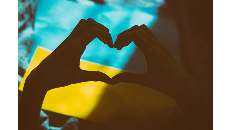 Heart shaped hands on Ukrainian flag with shadows. Vintage film photography. Ukrainian flag, creative patriotic. Stop the war in Ukraine. Stop Russian aggression. Stand with Ukraine