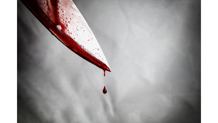 close-up of man holding knife smeared with blood and still dripping.