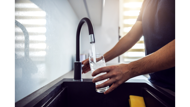 Close up of young man pouring fresh water from kitchen sink. Home interior.