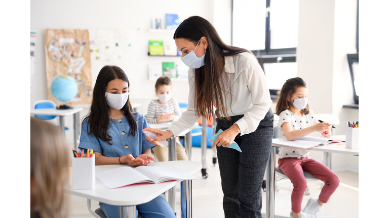 Teacher and children with face mask back at school, disinfecting hands.