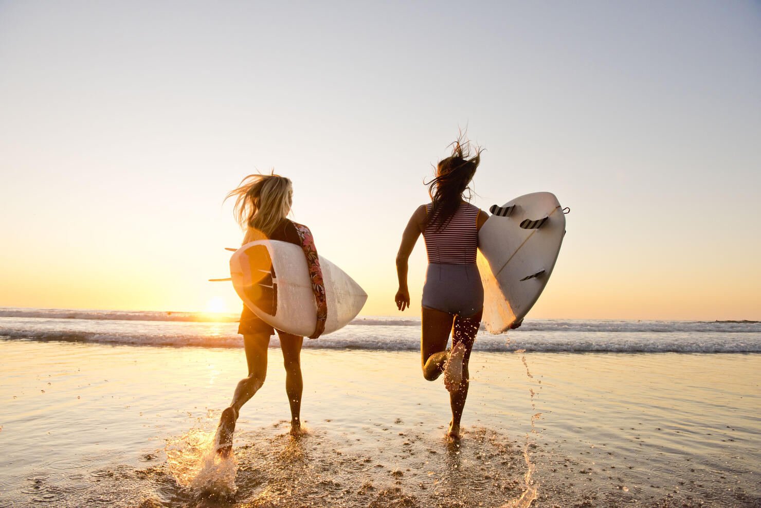 female surfers running on the beach at sunset