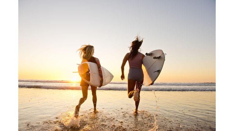 female surfers running on the beach at sunset