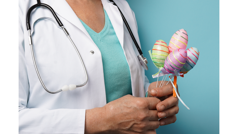 Doctor holding Easter painted eggs in her hands on blue background, medicine