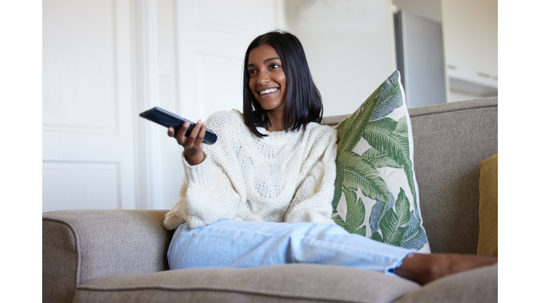 Shot of a beautiful young woman holding a remote control while sitting on the couch at home
