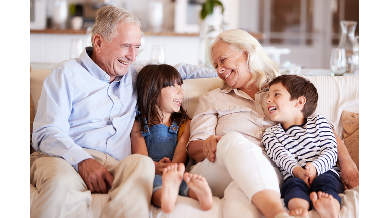 White senior couple and their grandchildren sitting on a sofa together smiling at each other