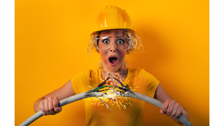 Worker girl with hat breaks an electric cable. Yellow background