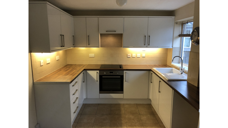 Image of empty rental property kitchen, magnolia painted walls, tiled flooring, oven, white cupboards with under lighting