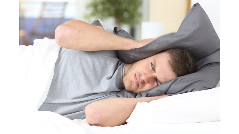 Man trying to sleep covering ears for noise