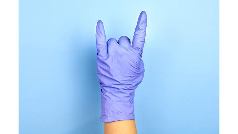 Female hand in medical gloves shows a rock gesture.