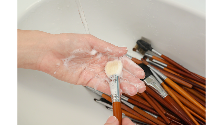 woman is washing dirty makeup brush with soap and foam in the sink