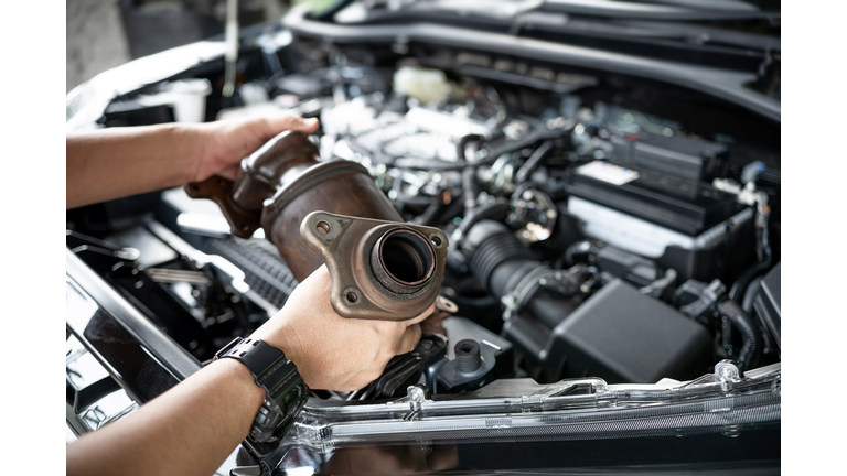 Close up old catalytic converter in hand Car service man remove from engine gasoline car dust clogged condition on filter in service concept and engine room in the background