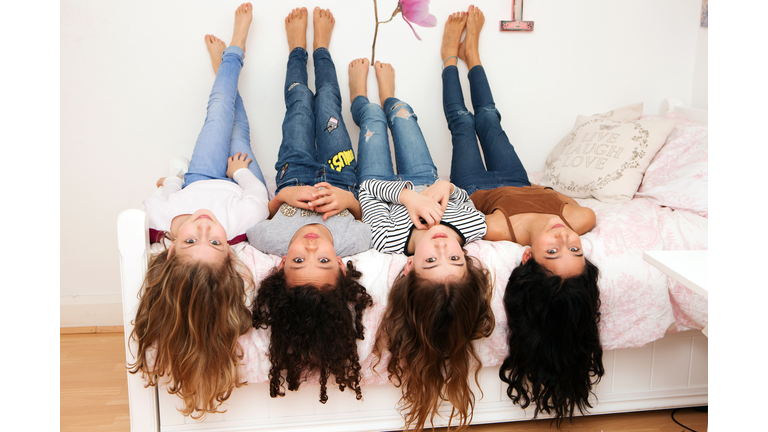 Girls lying upside down on bed looking at camera