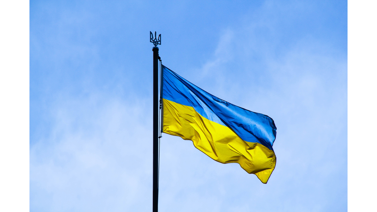 Ukrainian flag in the rays of the rising sun on a background of sky. Bicolor blue and yellow national flag of Ukraine on a flagpole and coat of arms of Ukraine trident. Official symbol of Ukraine