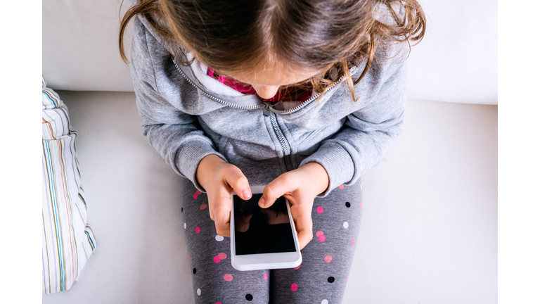 Little girl sitting on sofa, playing with smartphone