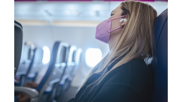 A millennial woman traveling by plane wears a protective face mask. ISL