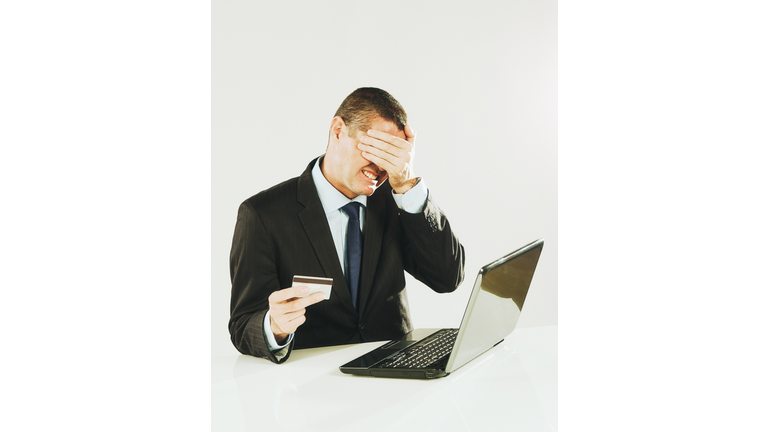 Buyer's remorse: Handsome man using laptop computer covers his face as he holds a credit card