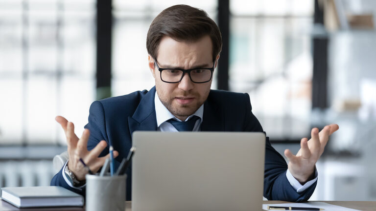 Angry male CEO frustrated by online problems working on laptop