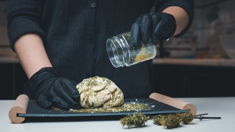 The young female chef preparing to cooking hemp cake or bread. Close-up of fresh dough with cannabis flour.