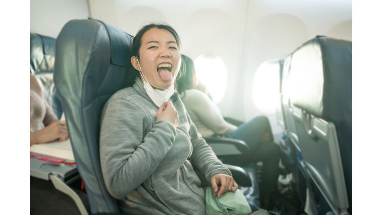Asian tourist woman flying in times of covid19 - young happy and excited Korean girl in face mask sitting on airplane cabin ready for flight  looking at the camera