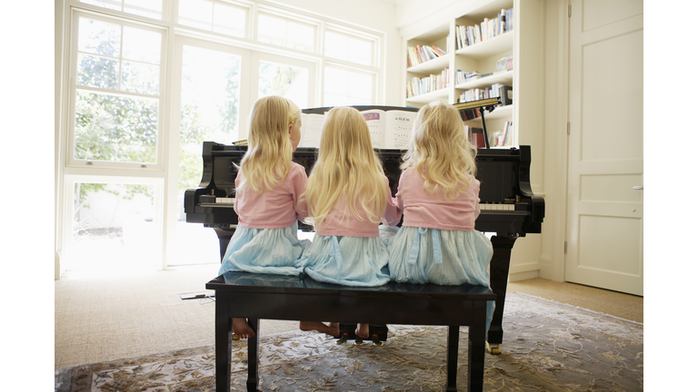 Rear View of Triplets Playing Piano in Living Room