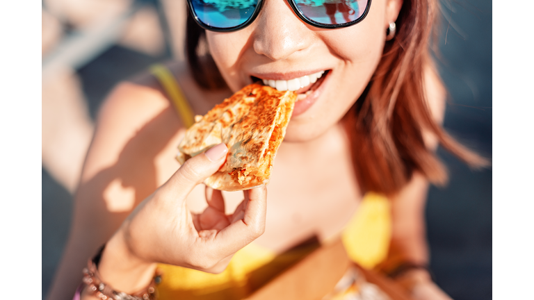 Happy girl eating Mexican fast food quesadilla on the beach. Healthy and tasty snack